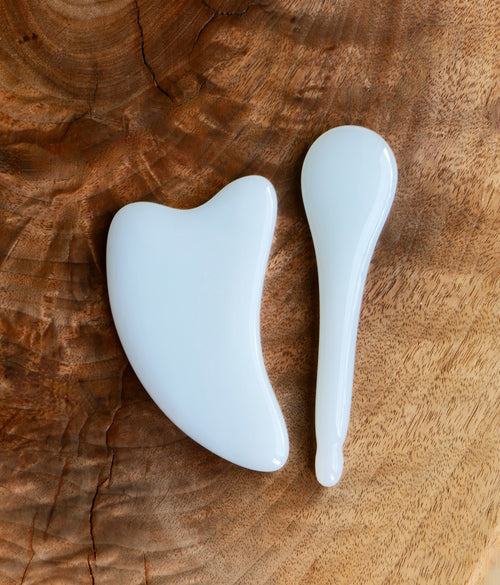 Front view of a standard dolphin-shaped jade gua sha next to a jade spoon-shaped gua sha 