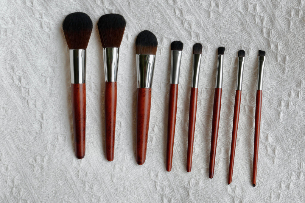 Front view of all 8 Makeup brushes laid out. There is a foundation, blush, contour, eye shadow, highlighter, eyeliner, concealer, waterline brush with wooden handles.