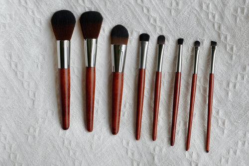 Front view of all 8 Makeup brushes laid out. There is a foundation, blush, contour, eye shadow, highlighter, eyeliner, concealer, waterline brush with wooden handles.