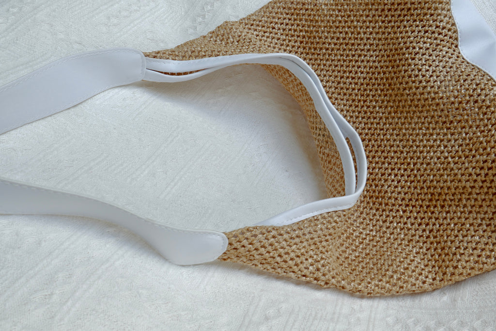The side view of a straw beach bag with white leather straps