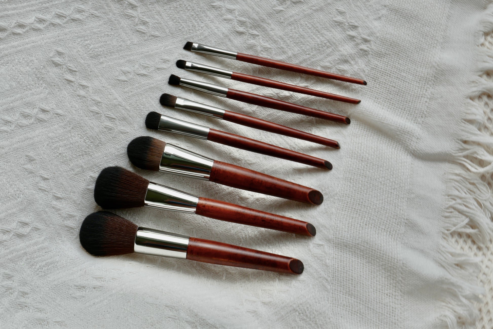 Side view of all 8 Makeup brushes laid out. There is a foundation, blush, contour, eye shadow, highlighter, eyeliner, concealer, waterline brush with wooden handles.