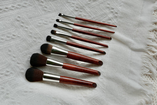 Side view of all 8 Makeup brushes laid out. There is a foundation, blush, contour, eye shadow, highlighter, eyeliner, concealer, waterline brush with wooden handles.